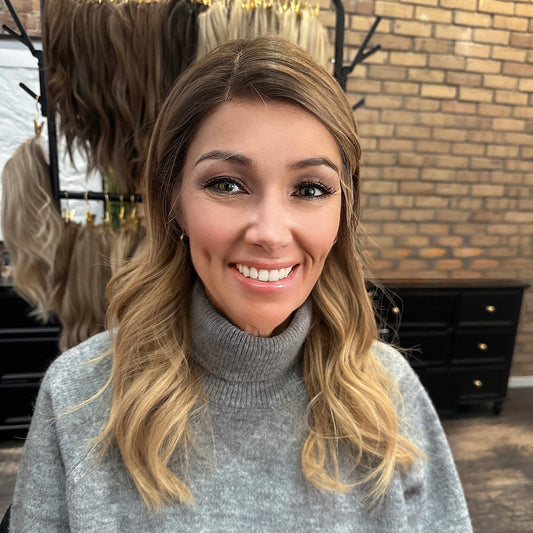 Kelly HD Wig by Jo Hair Studio – long layered brunette HD lace wig with blonde balayage highlights, styled in loose waves, hair tucked behind ears, front view in salon studio
